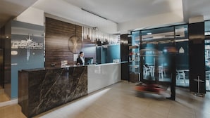 Una moderna recepción de hotel con mostrador de mármol, una recepcionista y un panel de vidrio que separa la recepción del comedor.