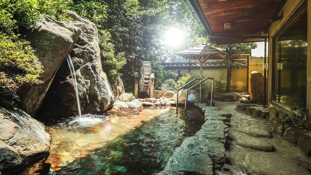 A serene outdoor area with a stone water feature, a wooden bridge, and a building with a traditional architectural style. - Nara Park Hotel (Nara)