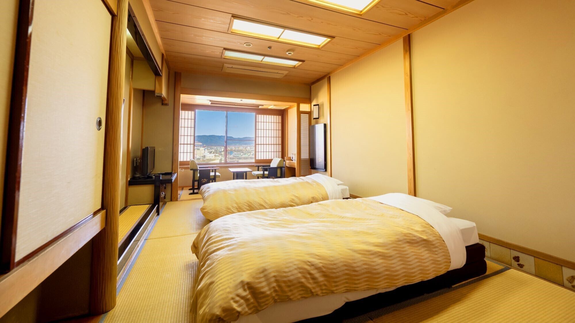 A hotel room with two beds, a desk, a chair, and a TV.