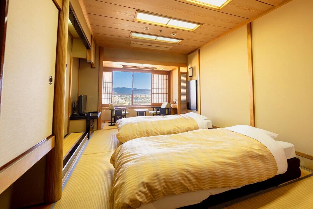 A hotel room with two beds, a desk, a chair, and a TV.