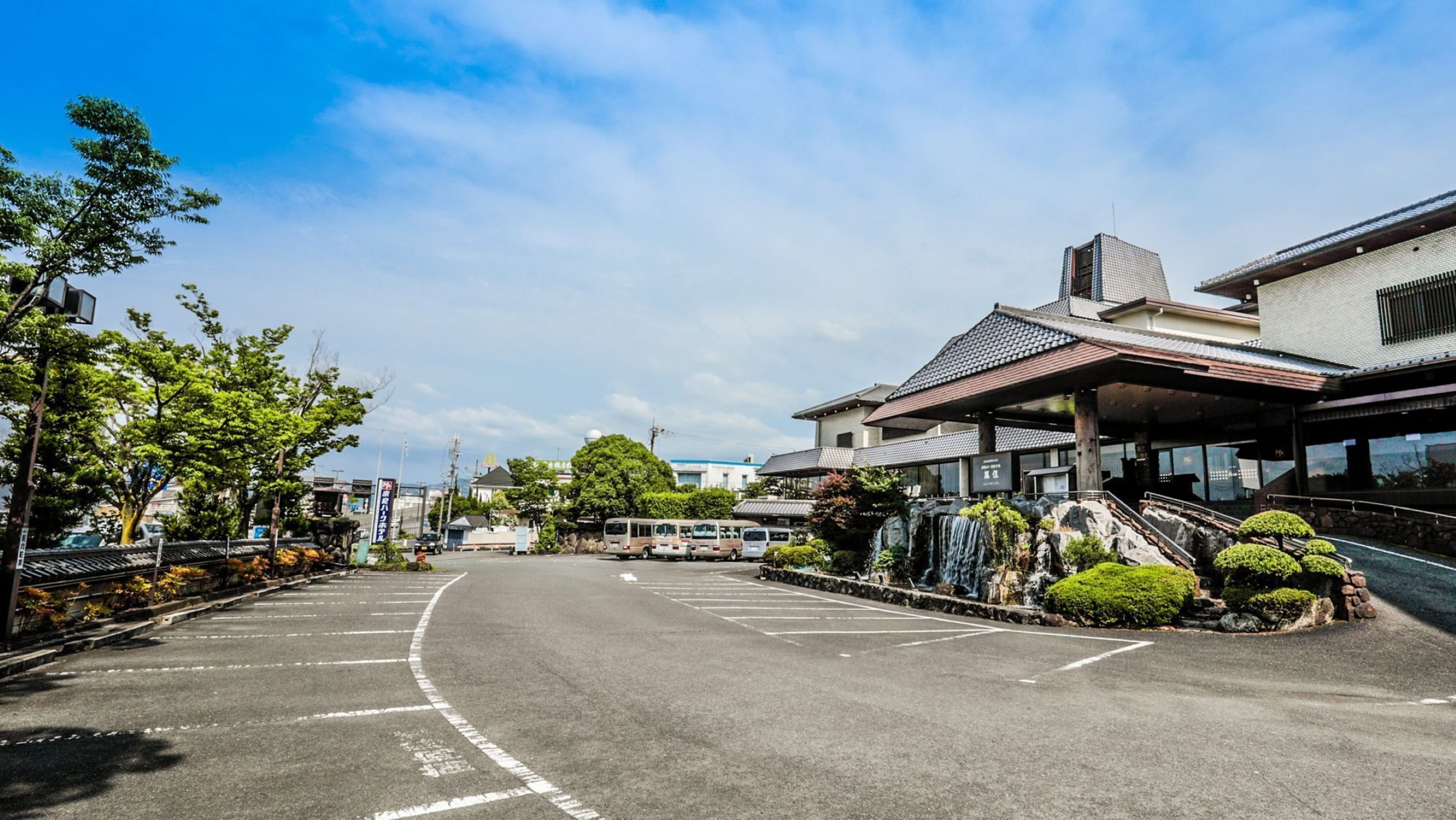 A parking lot with buses, a building with a traditional roof, and a waterfall.