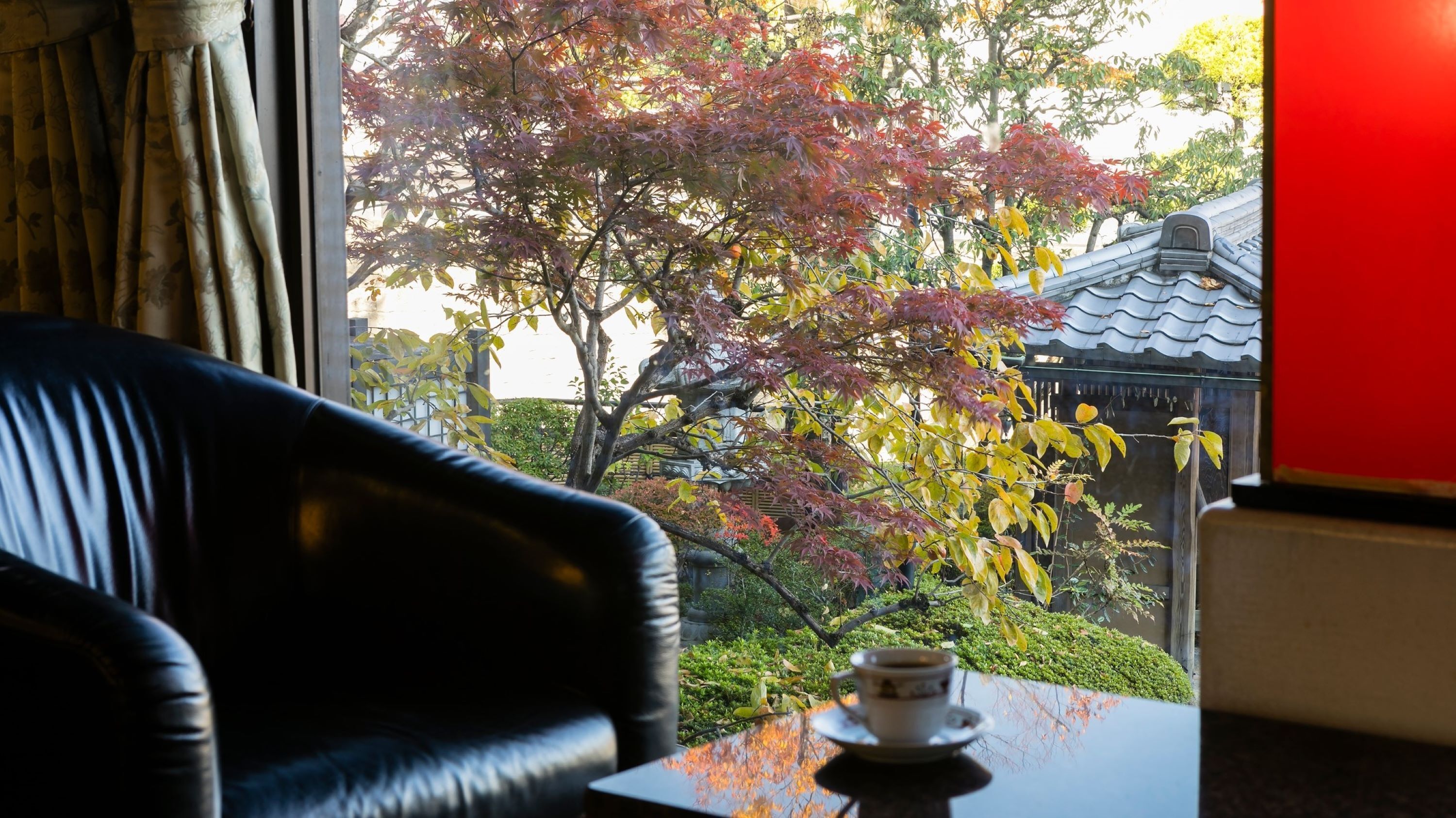 Ein Zimmer mit Gartenblick, ein Tisch mit Tasse und ein schwarzer Ledersessel.