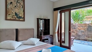 A hotel room with a bed, a nightstand, a mirror, and a painting on the wall. - Sapta Petala Hotel (Kuta)