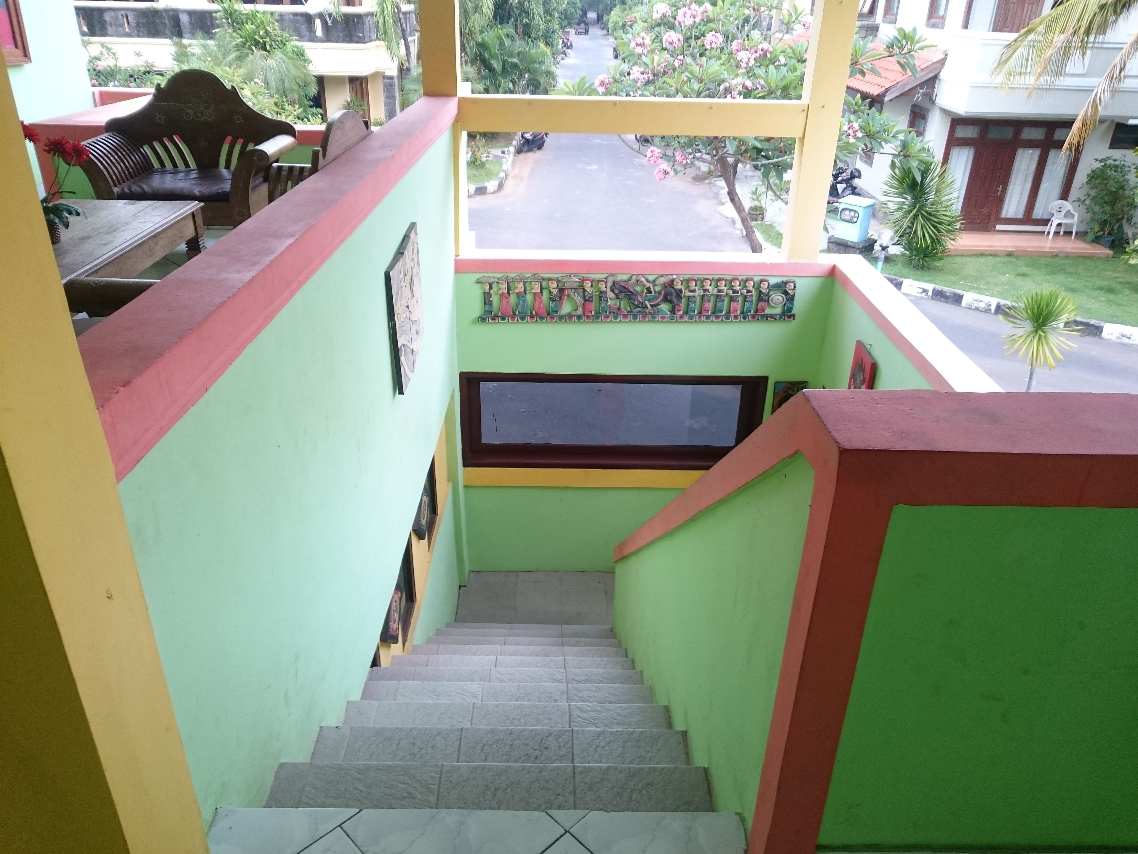 A staircase with green walls and a red border leading to a balcony with a view of a street and parked vehicles.