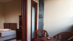 A bedroom with a bed, a wooden chair, a small table, and a stone pillar. - Sapta Petala Hotel (Kuta)