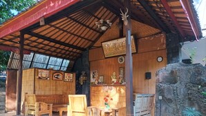 A wooden structure with a tiled floor, a large blue water dispenser, and several wooden chairs and tables. - Sapta Petala Hotel (Kuta)