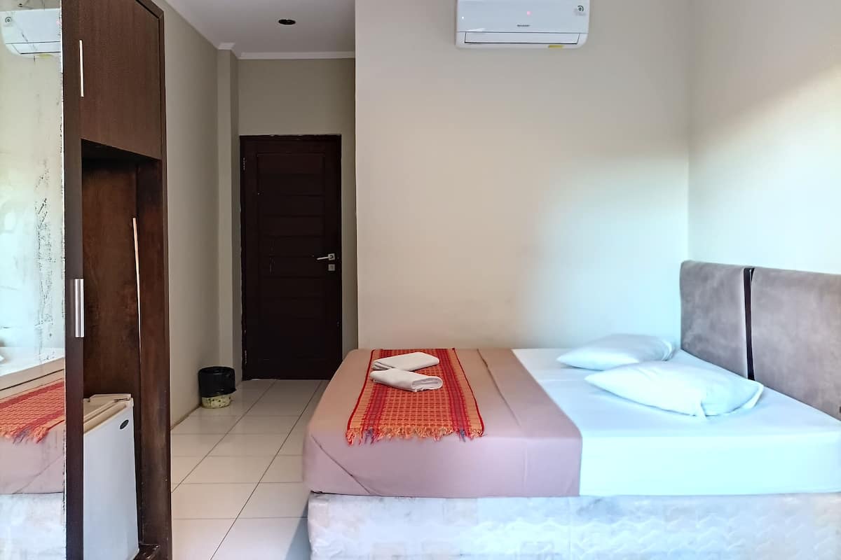 A hotel room with a bed, a bedside table, a wardrobe, and an air conditioning unit on the wall.