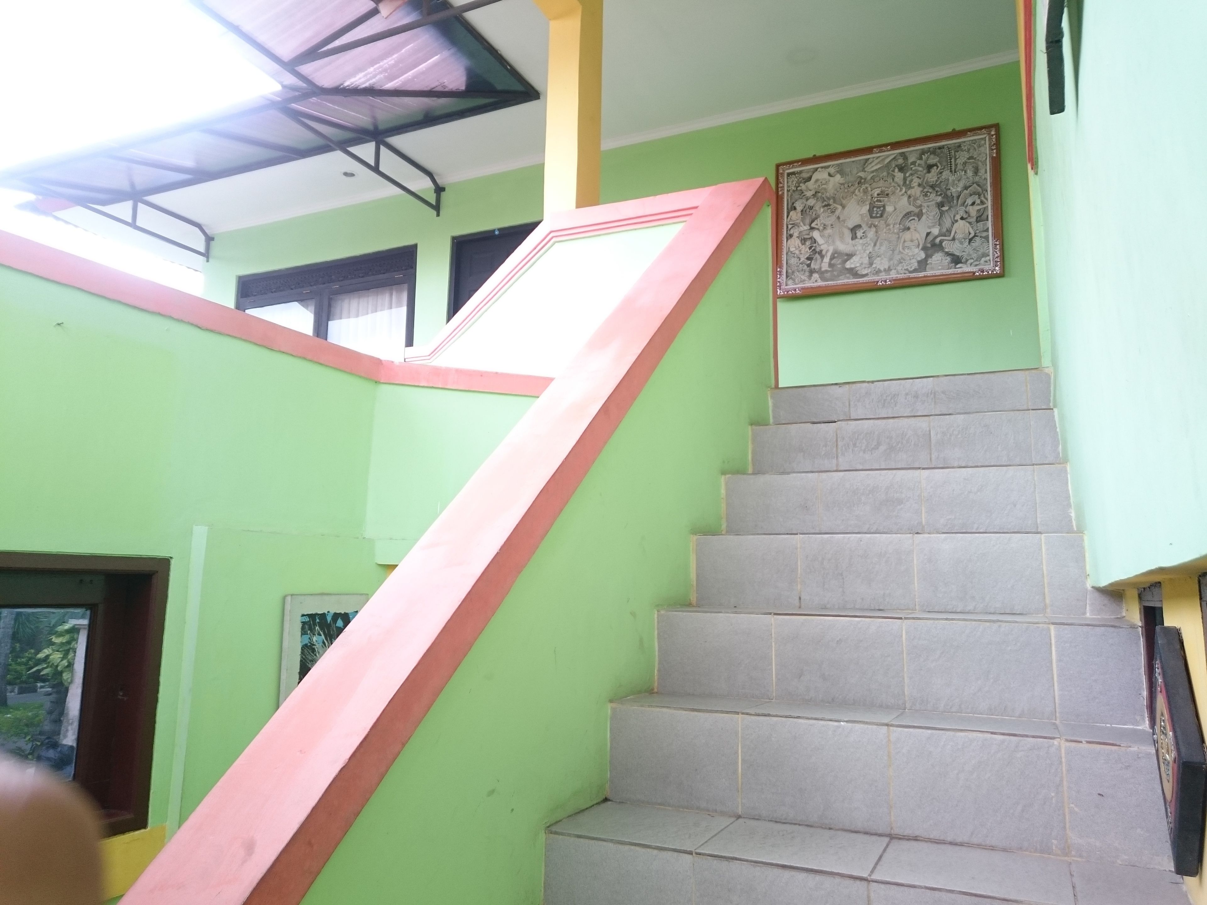 Una escalera con barandilla rosa que lleva a una plataforma, rodeada de paredes verdes y piso de baldosas.
