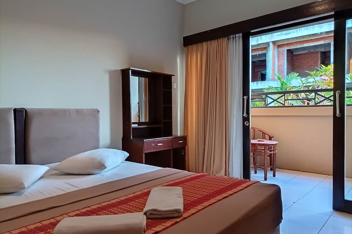 A hotel room with a bed, a desk, a mirror, and a balcony with plants.