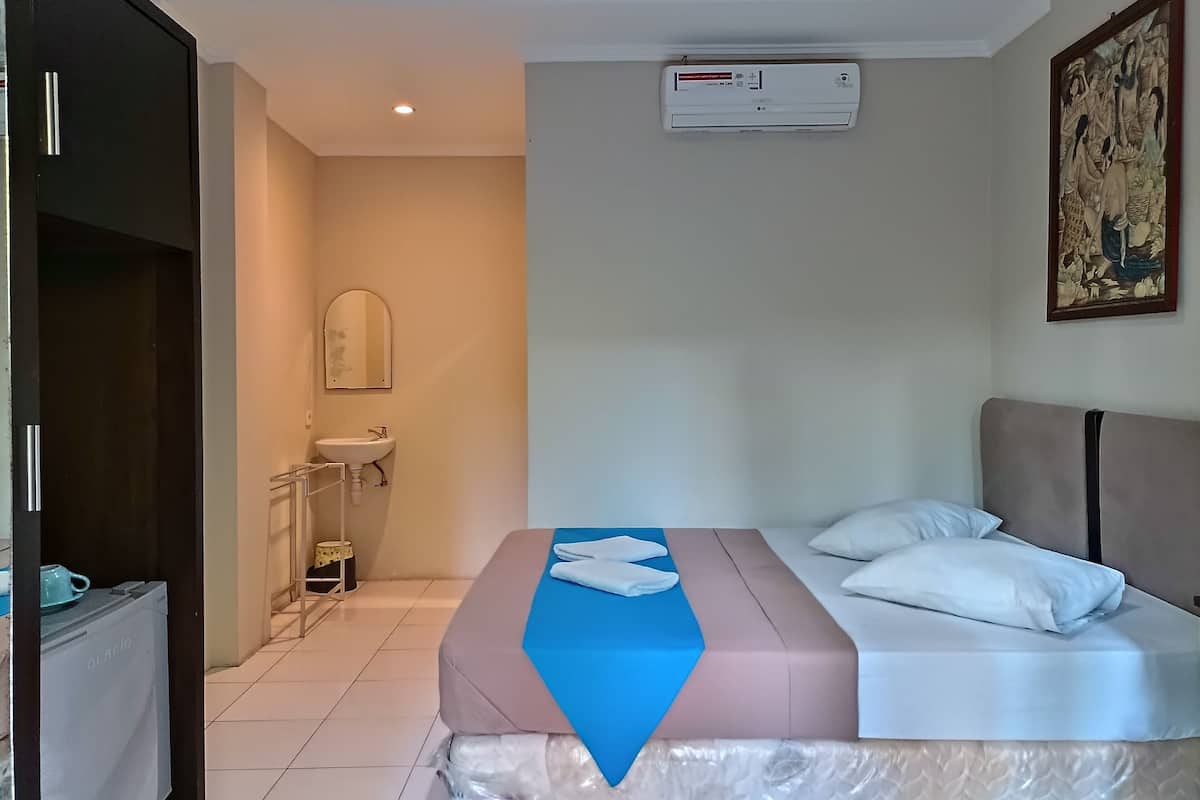 A hotel room with a bed, a sink, an air conditioner, and a painting on the wall.