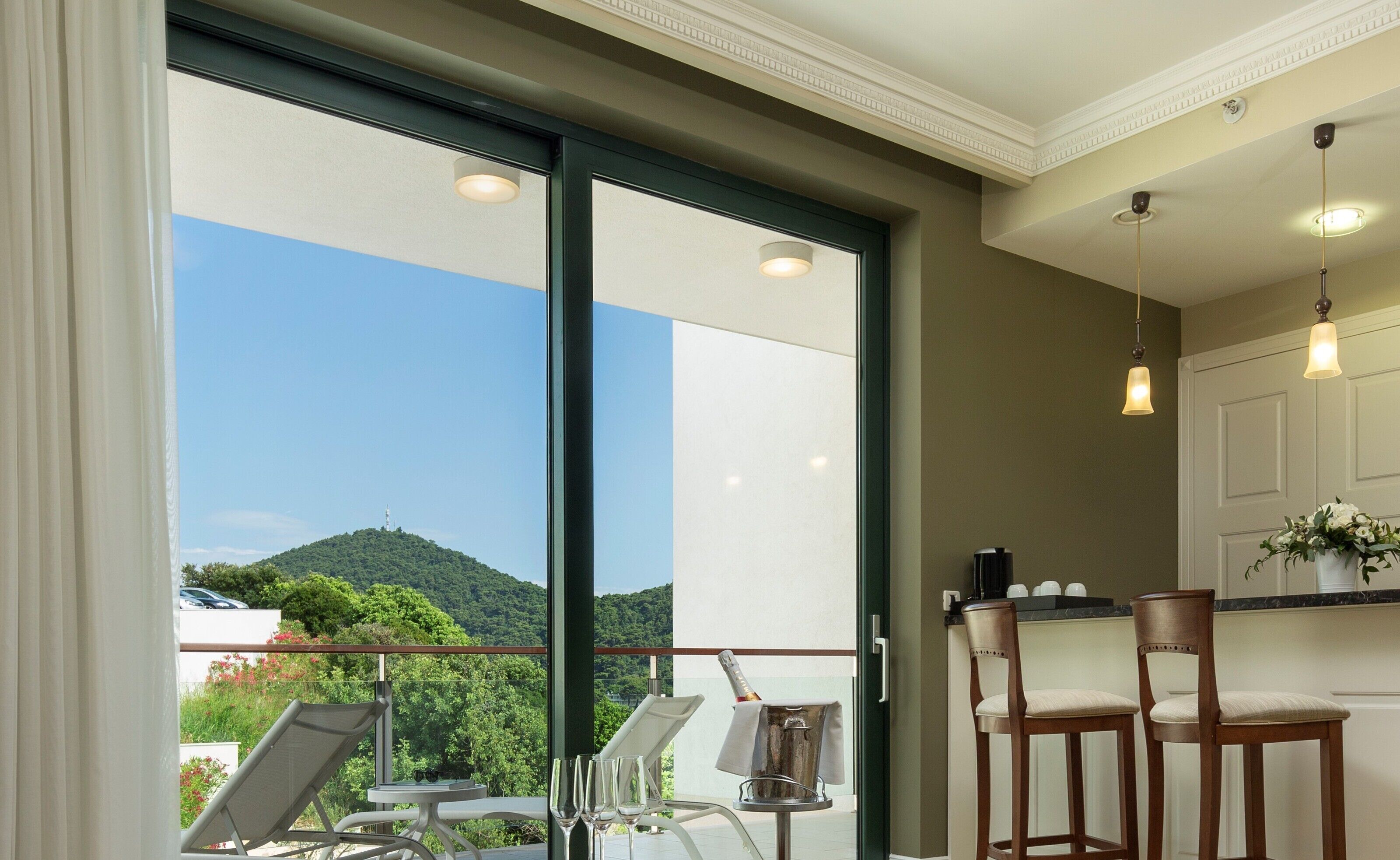 A balcony with a view of a green hill, a table with chairs, and a bar area with a bottle of champagne.
