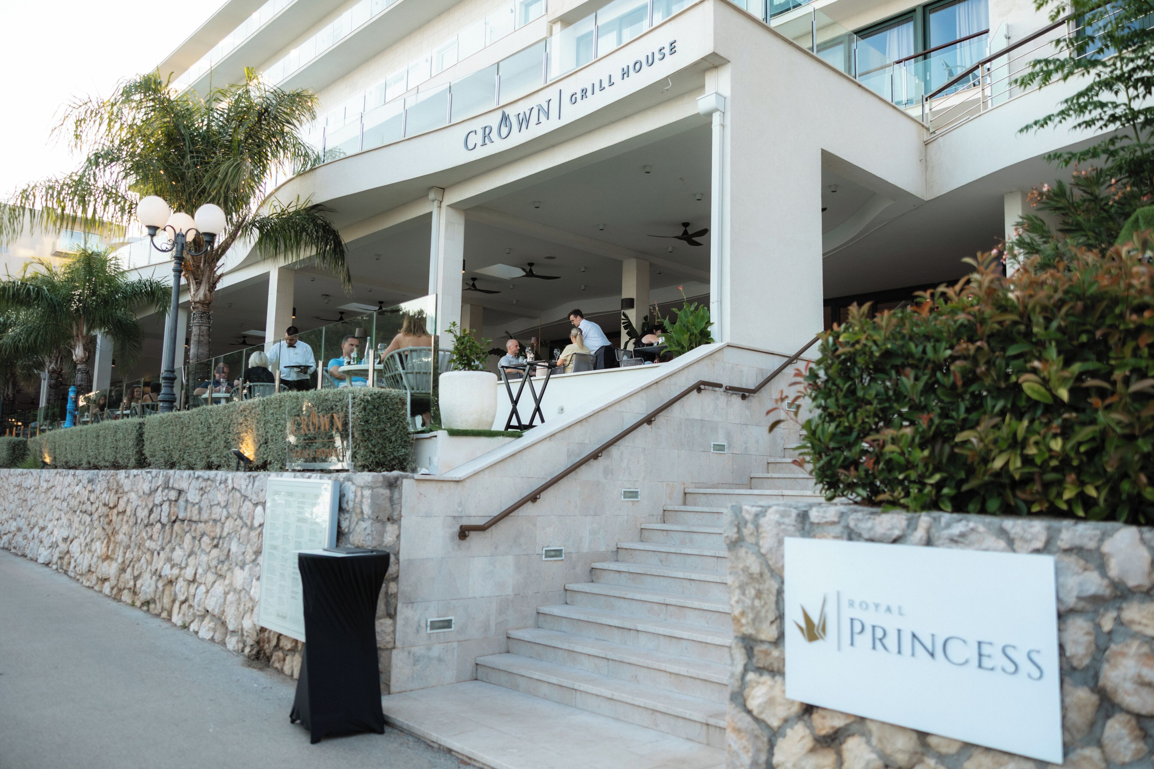 A hotel entrance with a sign reading 'Crown Grill House' and a sign for 'Royal Princess' on the stairs.