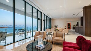 Amplia sala de estar con un gran ventanal que ofrece vistas al mar, un sofá rojo y una mesa de centro con libros.