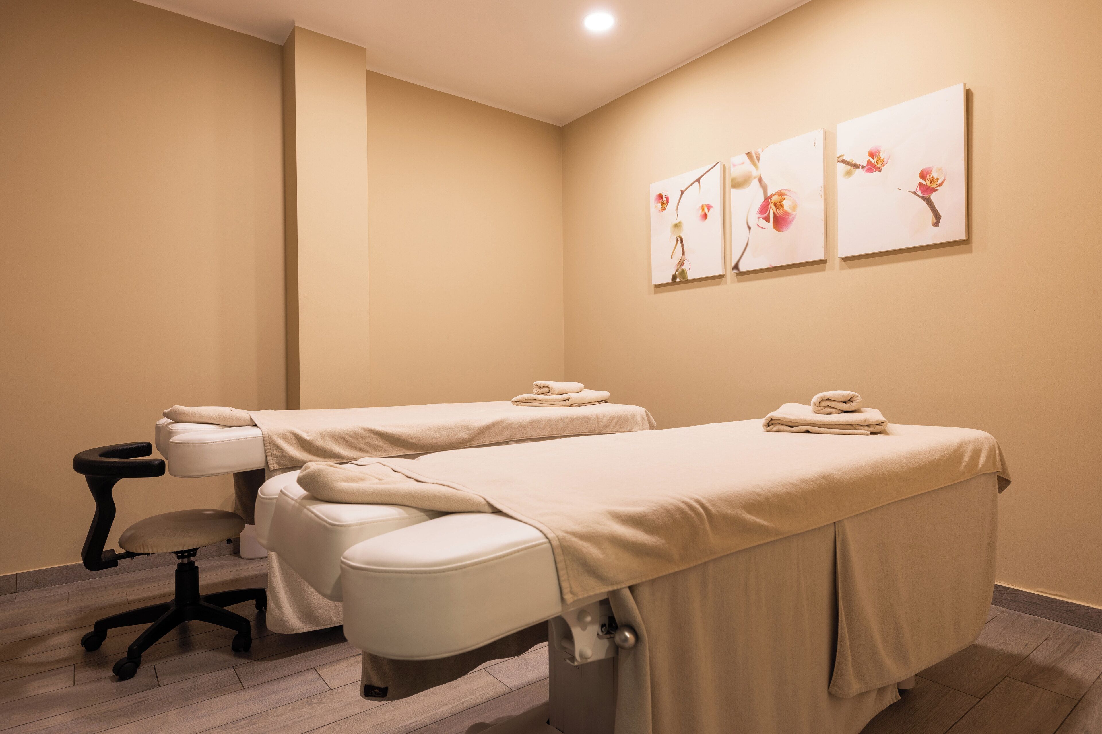 Un cuarto de spa con dos camillas de masaje, una mesita con una silla y obras de arte en las paredes.