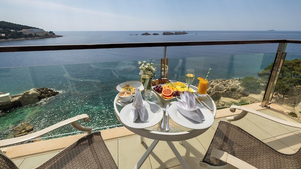 Una mesa con alimentos para el desayuno y una barandilla de vidrio con vista al mar.