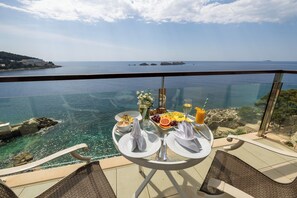 A table with breakfast items and a glass railing overlooking the sea. - Royal Princess Hotel (Dubrovnik)