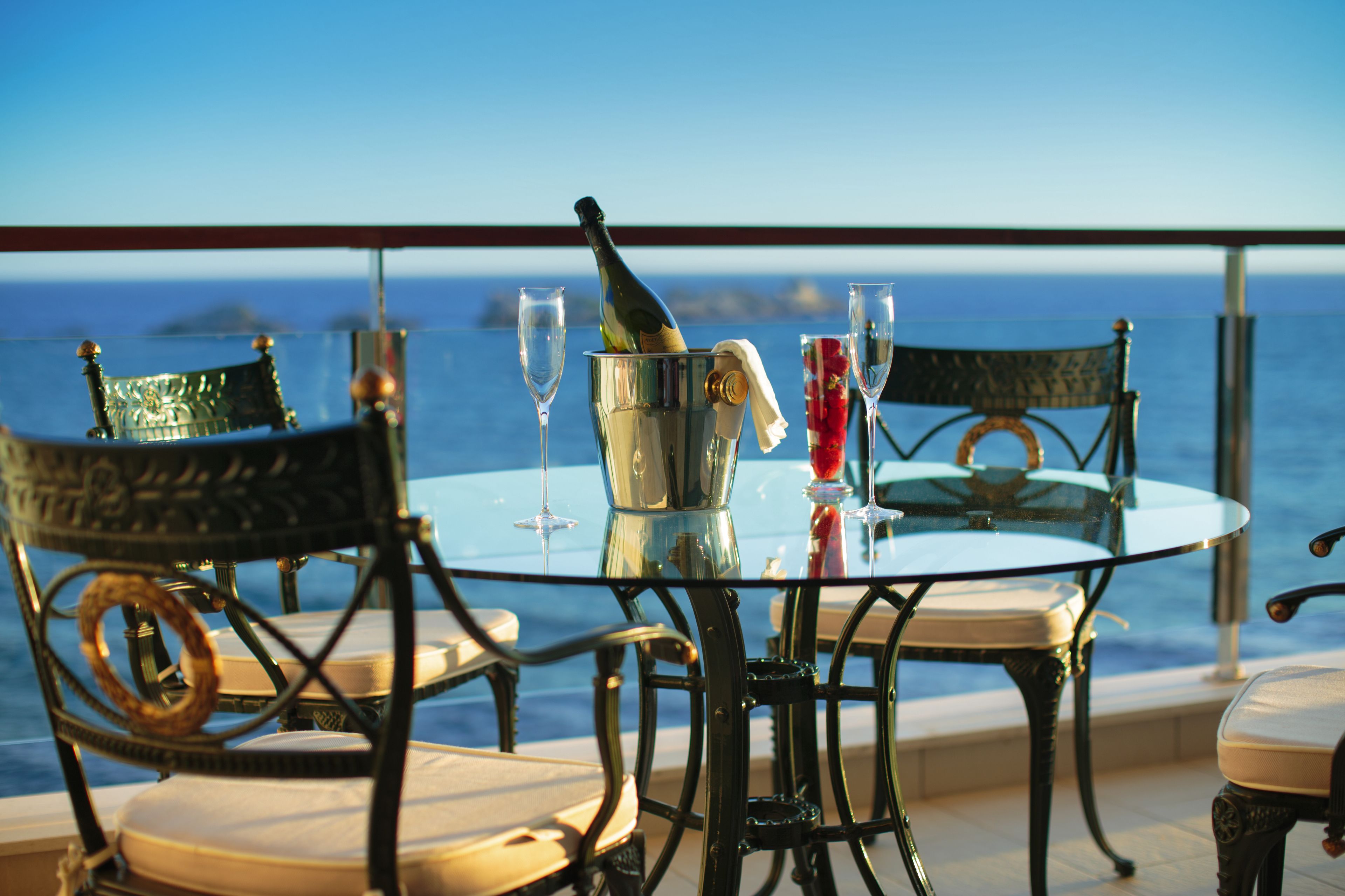Una mesa con sillas y una botella de champán, frente a una vista del mar.