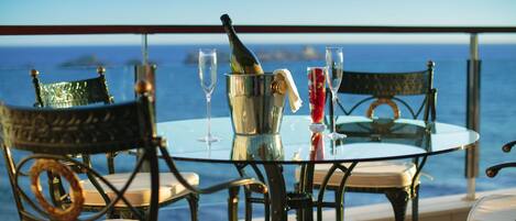 Una mesa con sillas y una botella de champán, frente a una vista del mar.