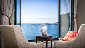 Habitación con un gran ventanal con vista al mar, con dos sillones, una mesita con un florero y una vista de islas distantes.