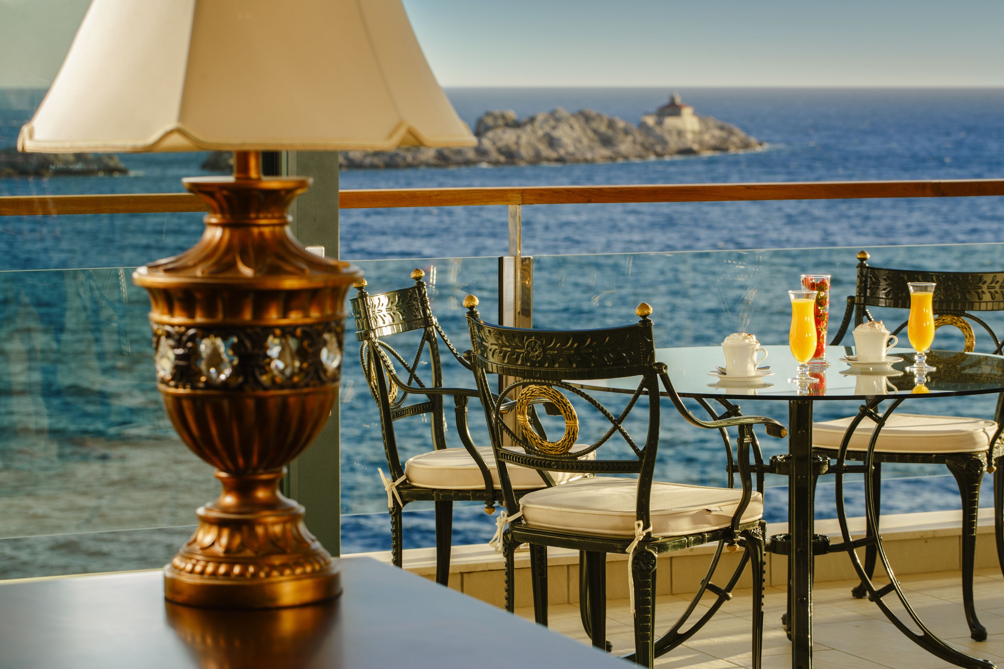 Una mesa con sillas y una lámpara, con vista a un cuerpo de agua y un promontorio rocoso en la distancia.