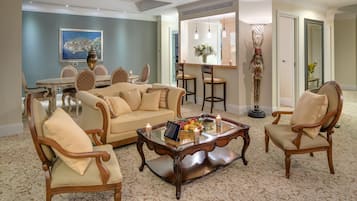 Un salón amplio con un sofá color beige, dos sillones, una mesa de centro con un frutero y velas, y un comedor con mesa y sillas.