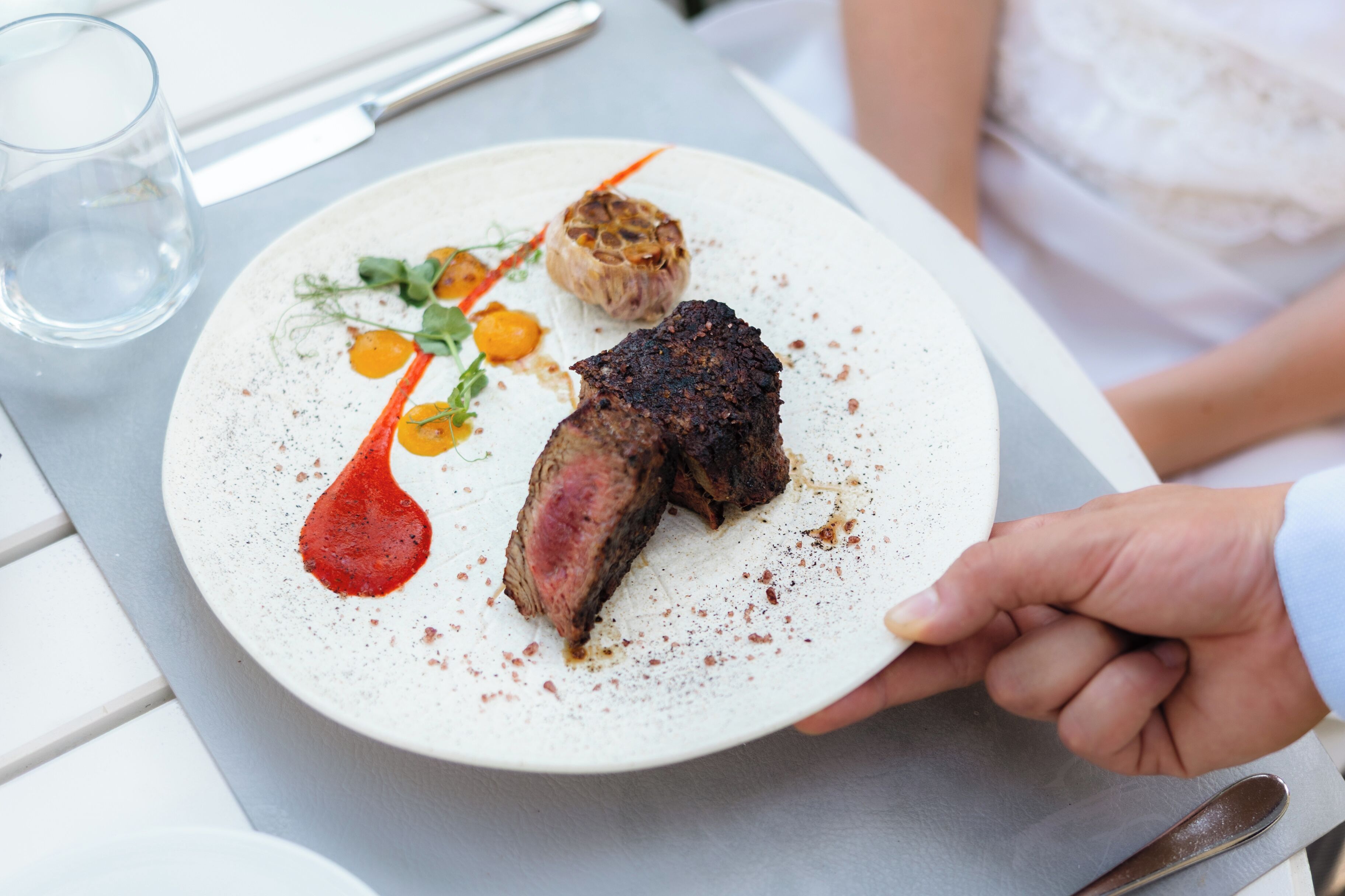 Un plato con un bistec, vegetales asados y una salsa.