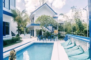 A pool area with a clear blue pool, blue chairs, and a staircase leading to a covered upper level. - Bombora Surf Camp (Pecatu)