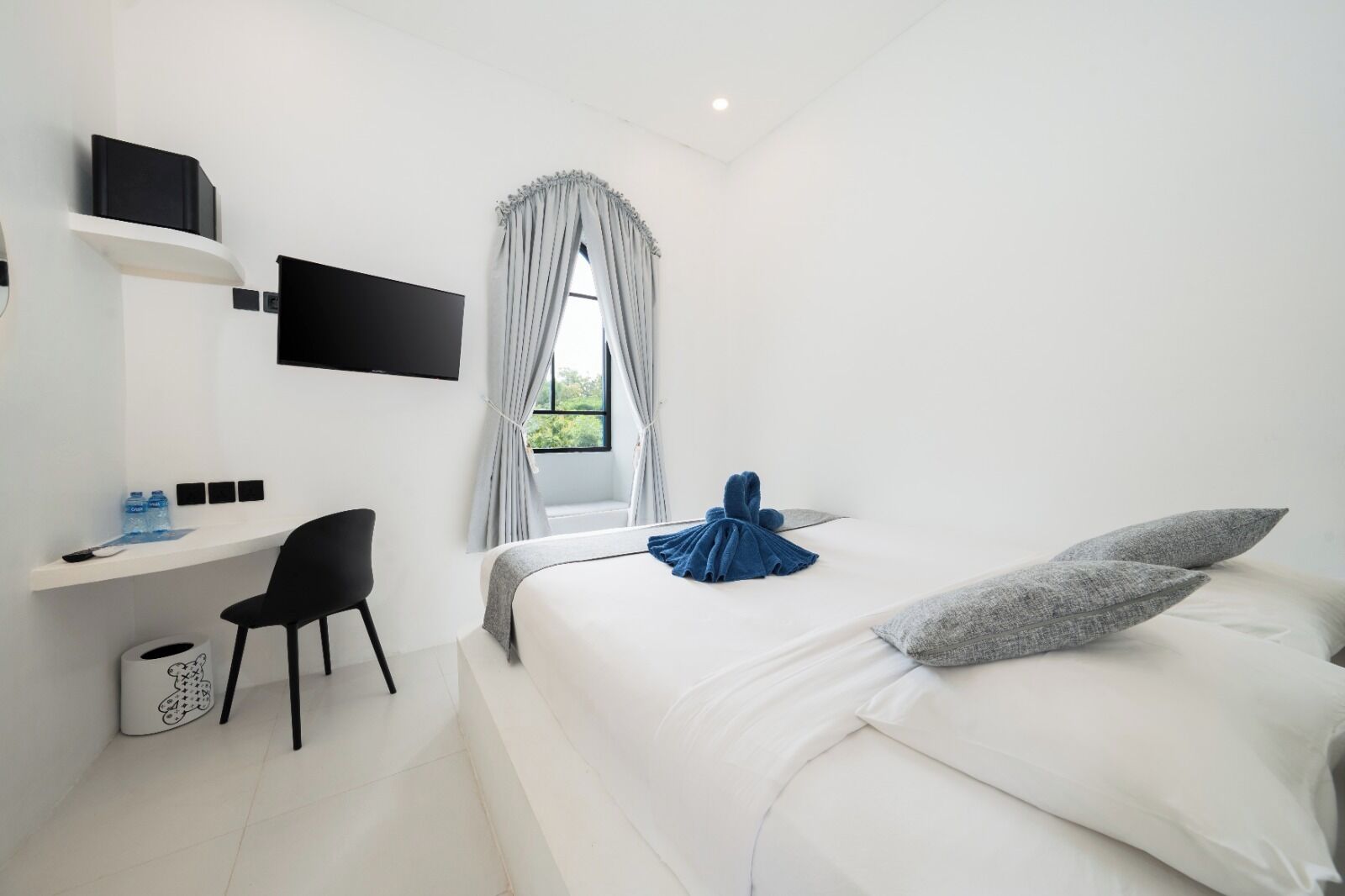 Una habitación de hotel moderna con cama, escritorio, silla, televisión y ventana con cortinas.