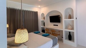 Une chambre d’hôtel moderne équipée d’un lit, d’une télévision, d’étagères et d’un luminaire suspendu.