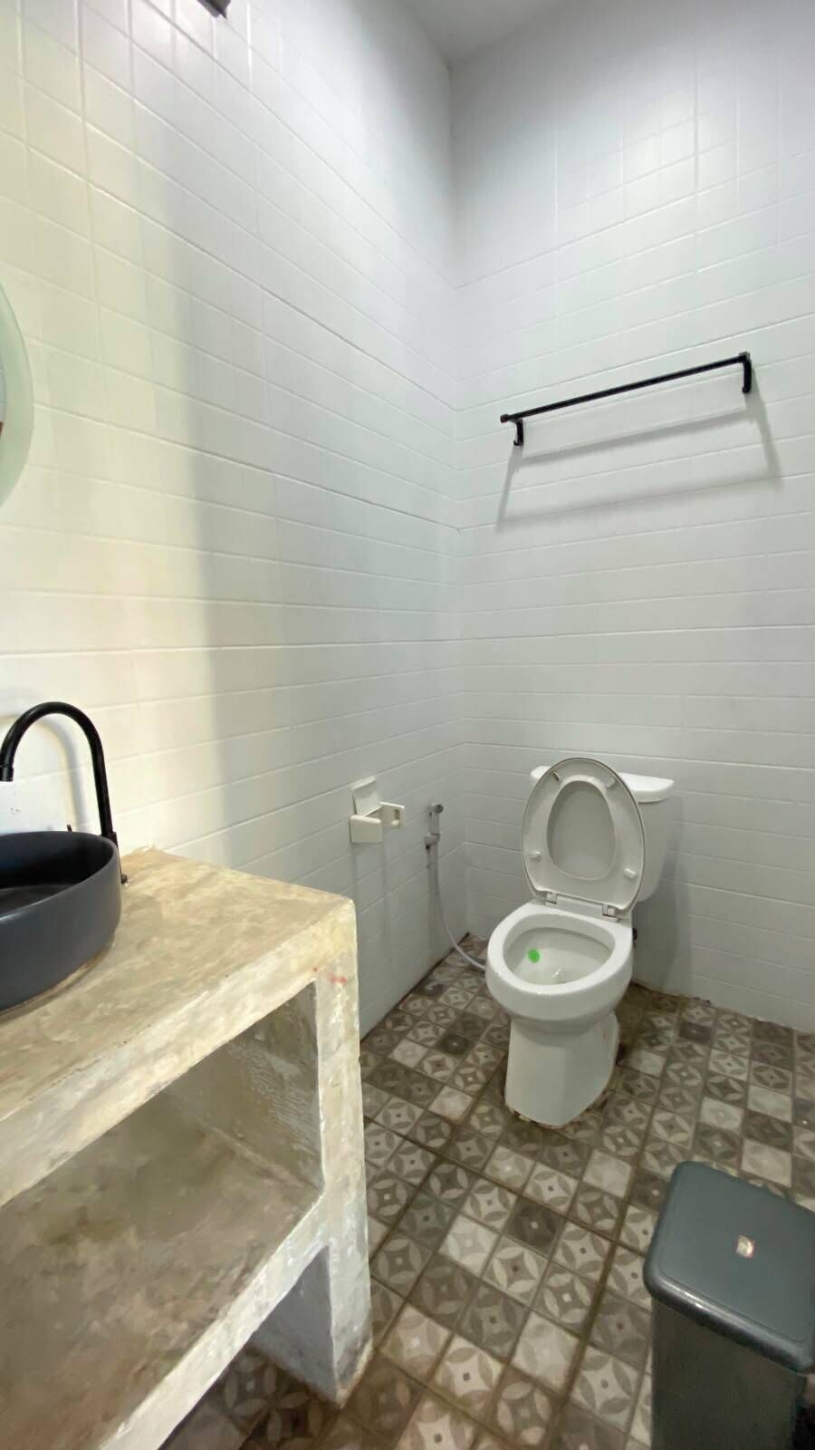 Ein Badezimmer mit weißen Fliesen, einer Toilette, einem Waschbecken und einem Mülleimer.