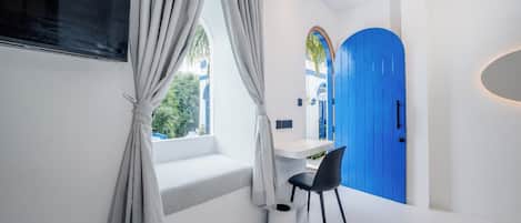 A modern room with a white desk, a black chair, a blue door, and a window with curtains.