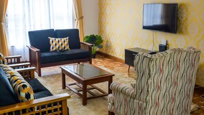 Un soggiorno con divano, poltrone, tavolino, televisore e parete decorata.