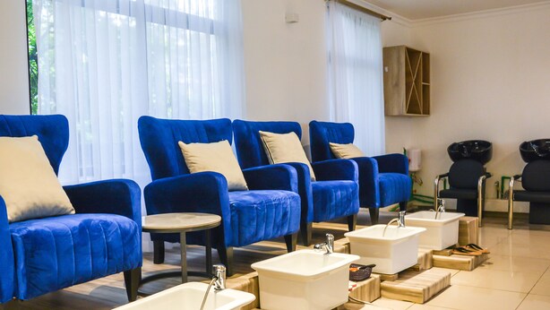 Un'area spa moderna con poltrone blu, lavabi bianchi e poggiapiedi in legno.