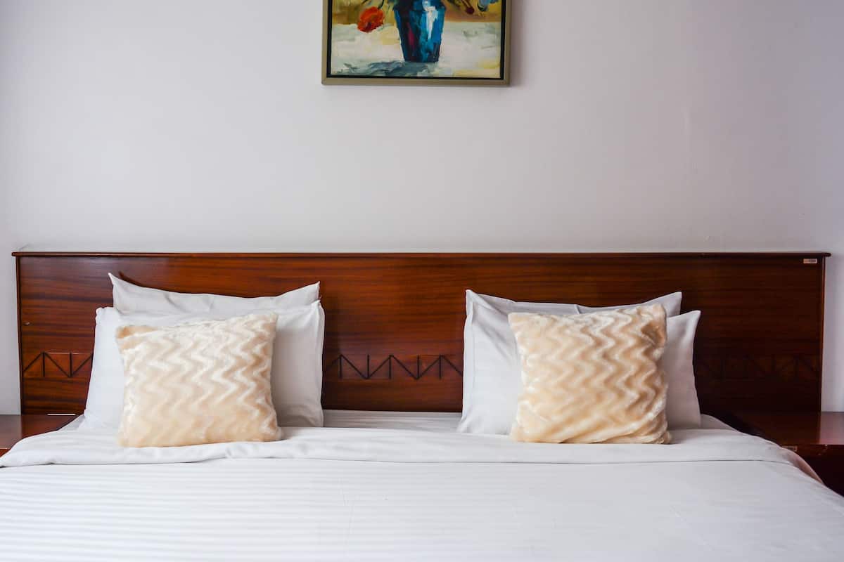 Una cama bien hecha con cabecera de madera, dos almohadas estampadas y un cuadro sobre la cama.