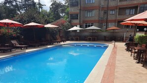 Una piscina con lettini e ombrelloni, circondata da un edificio con numerose finestre.