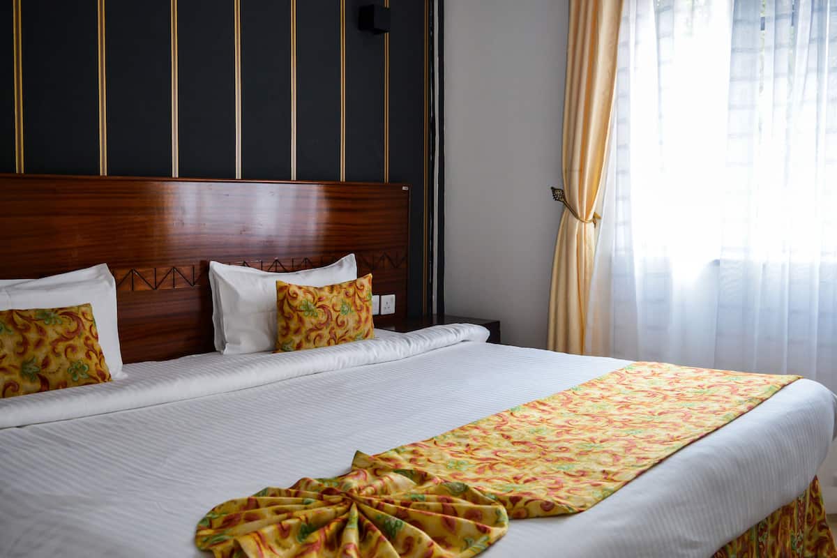 Una cama bien tendida con sábanas blancas y una manta decorativa, un cabecero de madera y una ventana con cortinas.