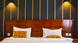 Una camera d'albergo con una testiera in legno, due cuscini bianchi, una coperta colorata e lampade a parete.