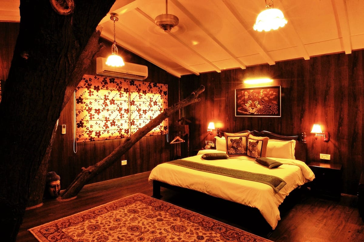 A cozy room with a large bed, wooden walls, a decorative tree trunk, and a patterned rug.