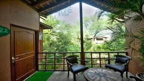 A balcony with two chairs and a table, a wooden door, and a view of greenery. - The Tree House Resort (Amer)