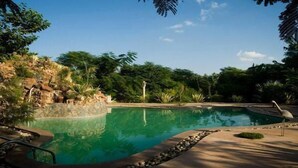 A swimming pool surrounded by natural rock formations and greenery. - The Tree House Resort (Amer)