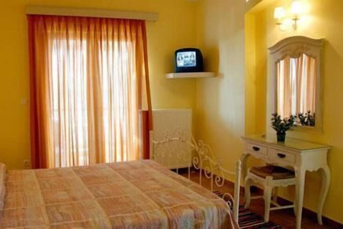 Ein Hotelzimmer mit einem Bett, einem Fernseher auf einem Regal, einem Schminktisch und einem Spiegel.
