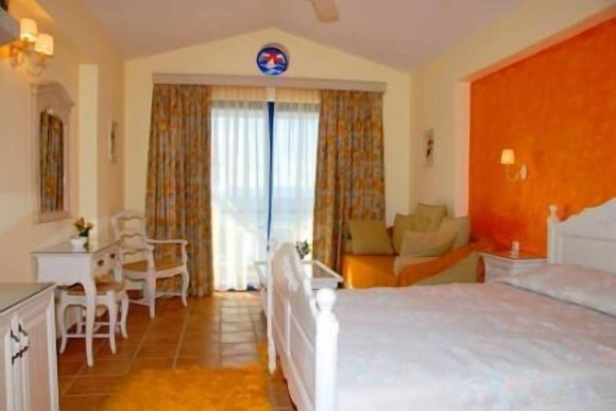 Ein Hotelzimmer mit Bett, Schreibtisch und Stuhl. Ein Fenster mit Vorhängen bietet Blick ins Freie.