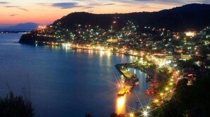 A coastal town at dusk with illuminated buildings and a calm sea. - Agnadi Hotel (Mantoudi-Limni-Agia Anna)