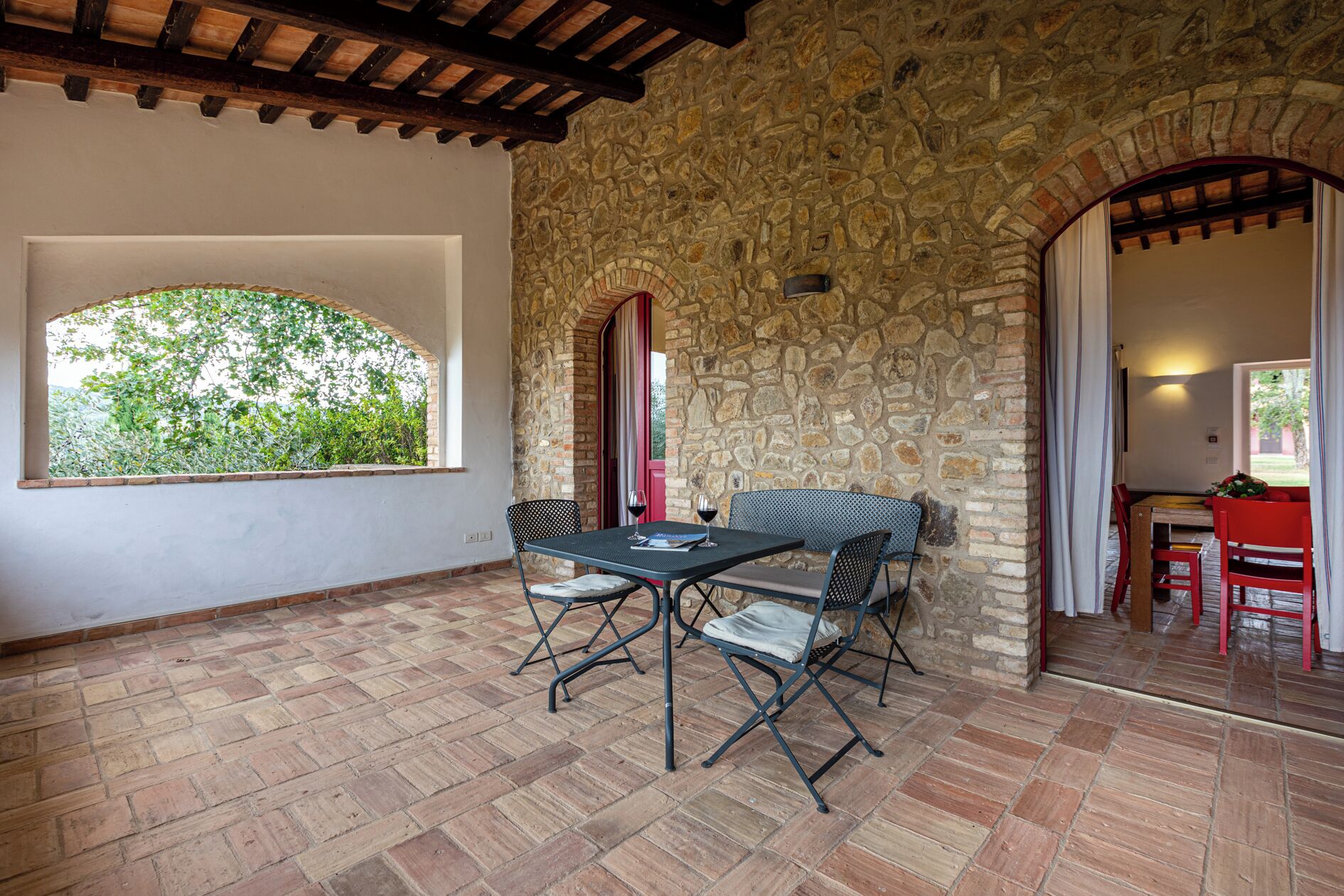 Un patio con pareti in pietra, un tavolo e sedie, una finestra con vista sul verde e un ingresso che dà su un'altra stanza.