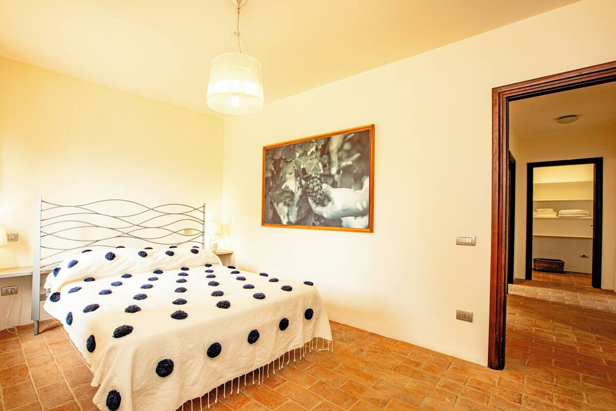A bedroom with a bed, a hanging light fixture, a framed picture, and a brick floor.