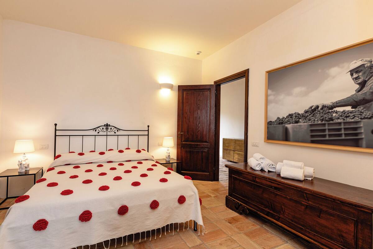 A bedroom with a bed, bedside lamps, a wooden dresser, a mirror, and a framed picture on the wall.