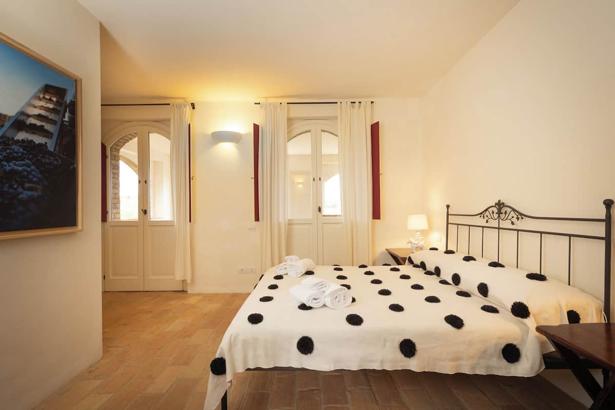A hotel room with two beds, a wooden floor, a painting on the wall, and a window with curtains.