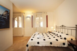 Quarto de hotel com duas camas, piso de madeira, um quadro na parede e uma janela com cortinas.