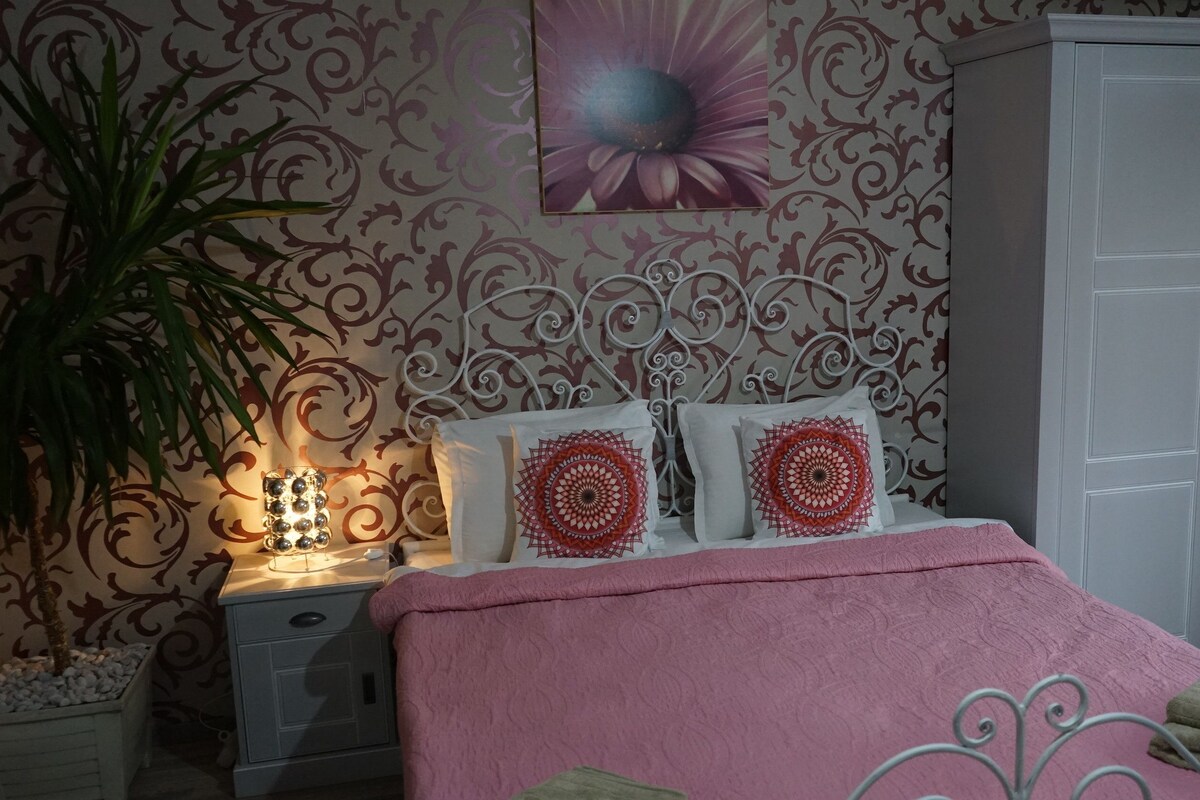 Et soveværelse med seng, sengebord, lampe, pyntemæssige puder, et klædeskab og en væg med blomstermønster.