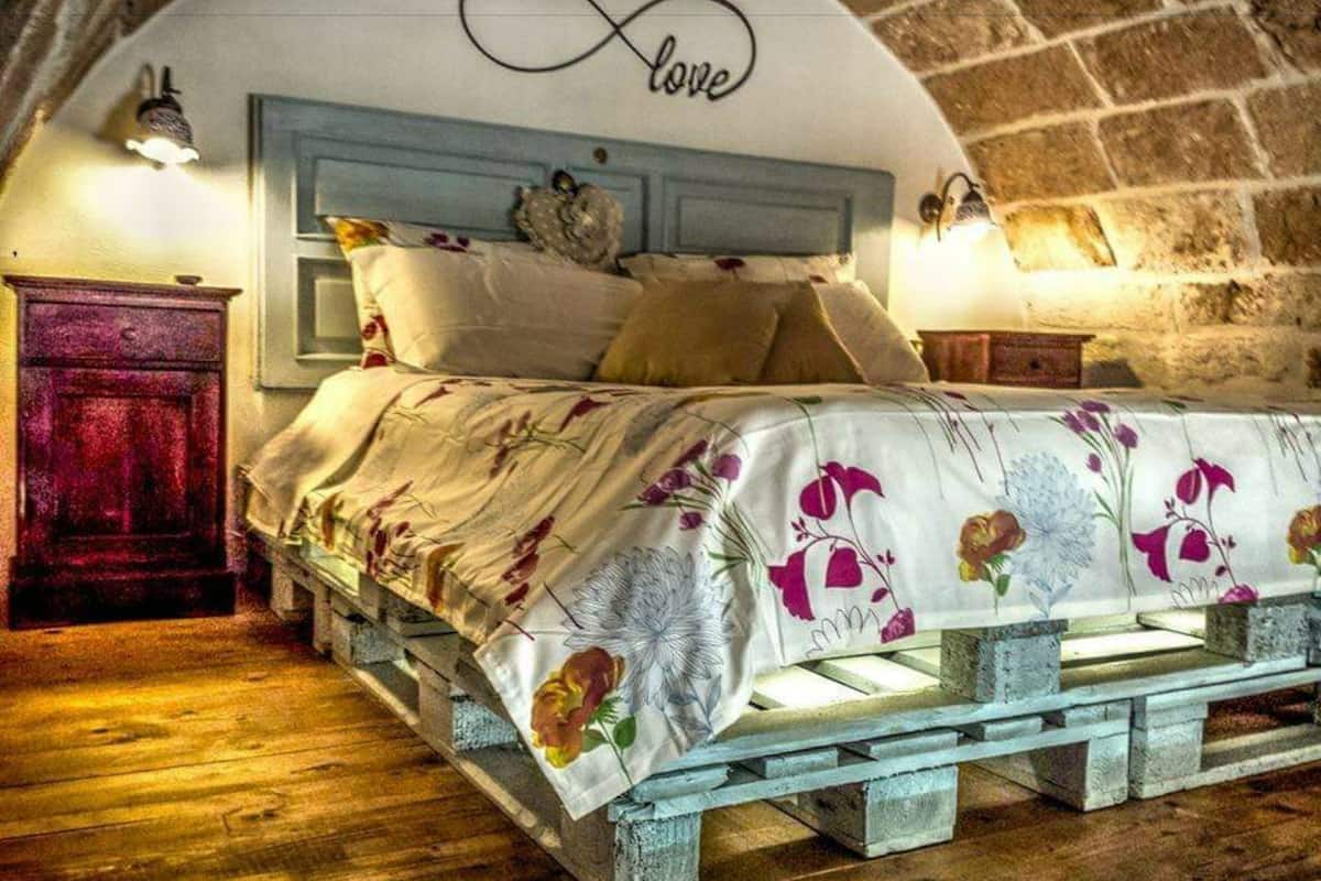 Un dormitorio rústico con estructura de cama de madera, ropa de cama floral y una pared de piedra curva.